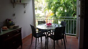 Ein Balkon mit Tisch und Stühlen, einem Deckenventilator und Blick auf üppiges Grün.