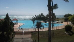 Ein Poolbereich mit Blick auf das Meer, umgeben von Palmen und einer eingezäunten Terrasse.