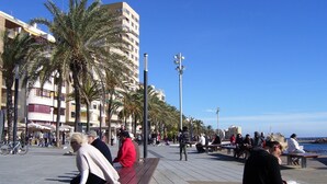 A public square with benches, palm trees, and people sitting and walking. - 2-bedroom apartment community pool WIFI close to beaches (TORREVIEJA)