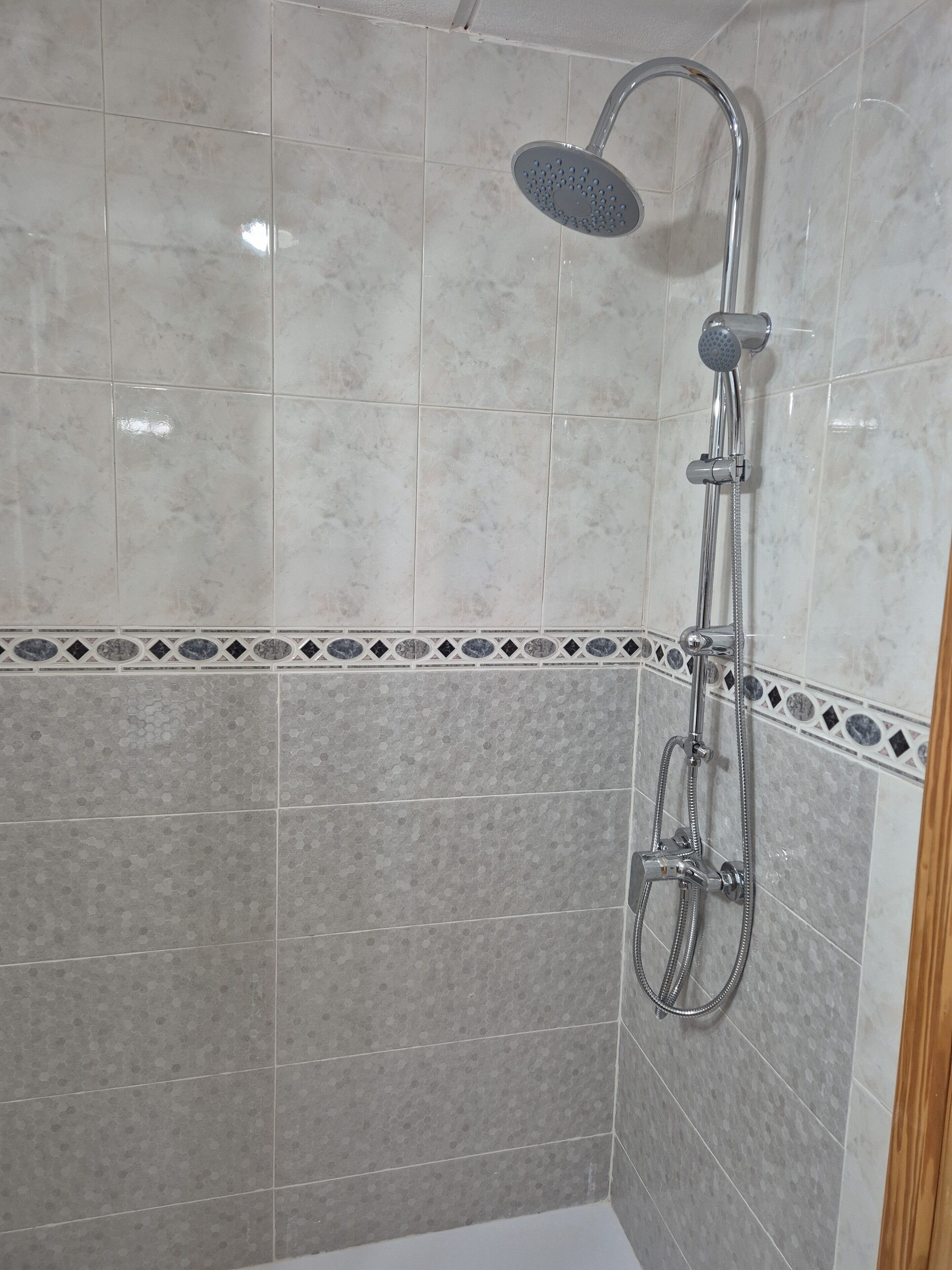 Een douche met een handdouche en een wandmengkraan.