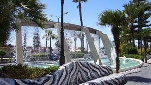 A public fountain with a mosaic bench, surrounded by palm trees and a clear sky. - 2-bedroom apartment community pool WIFI close to beaches (TORREVIEJA)