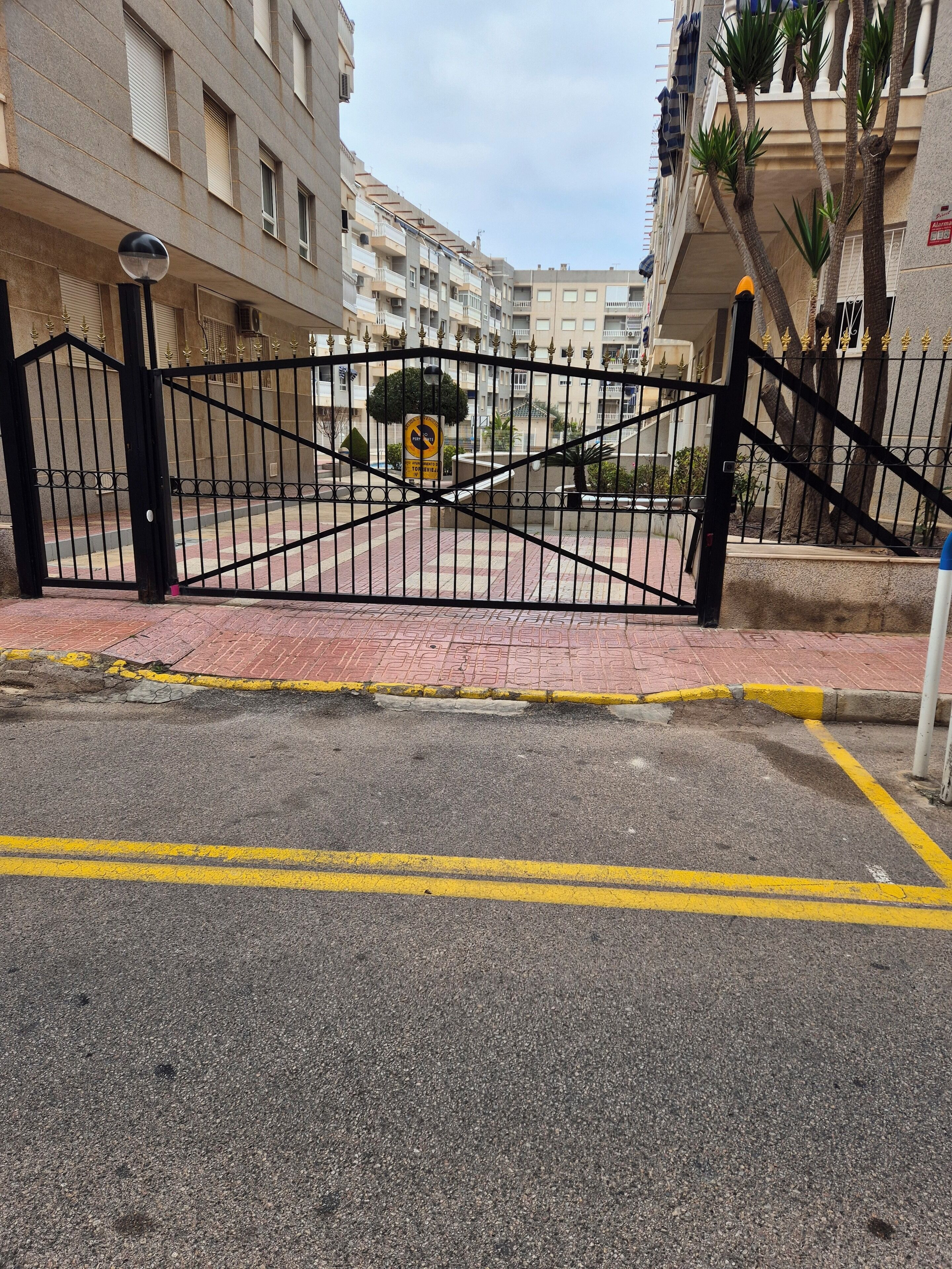 A gated entrance to a residential building with a paved pathway and a yellow line marking.