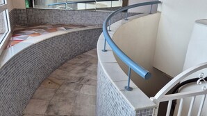 A curved staircase with a metal handrail, tiled walls, and a metal gate at the bottom. - 2-bedroom apartment community pool WIFI close to beaches (TORREVIEJA)