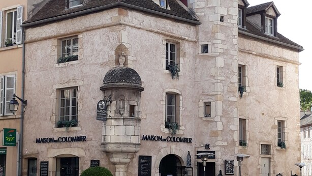 Un edificio histórico con una torre central, múltiples ventanas y un letrero que dice 'MAISON COLOMBIER'.