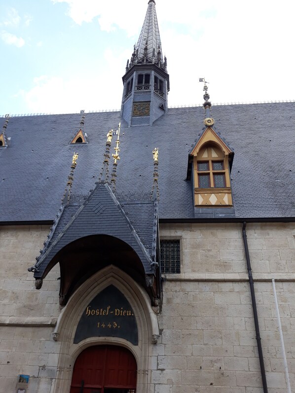 A building with a pointed roof, a clock tower, and a sign reading 'Hostel-Vieu 1443.'
