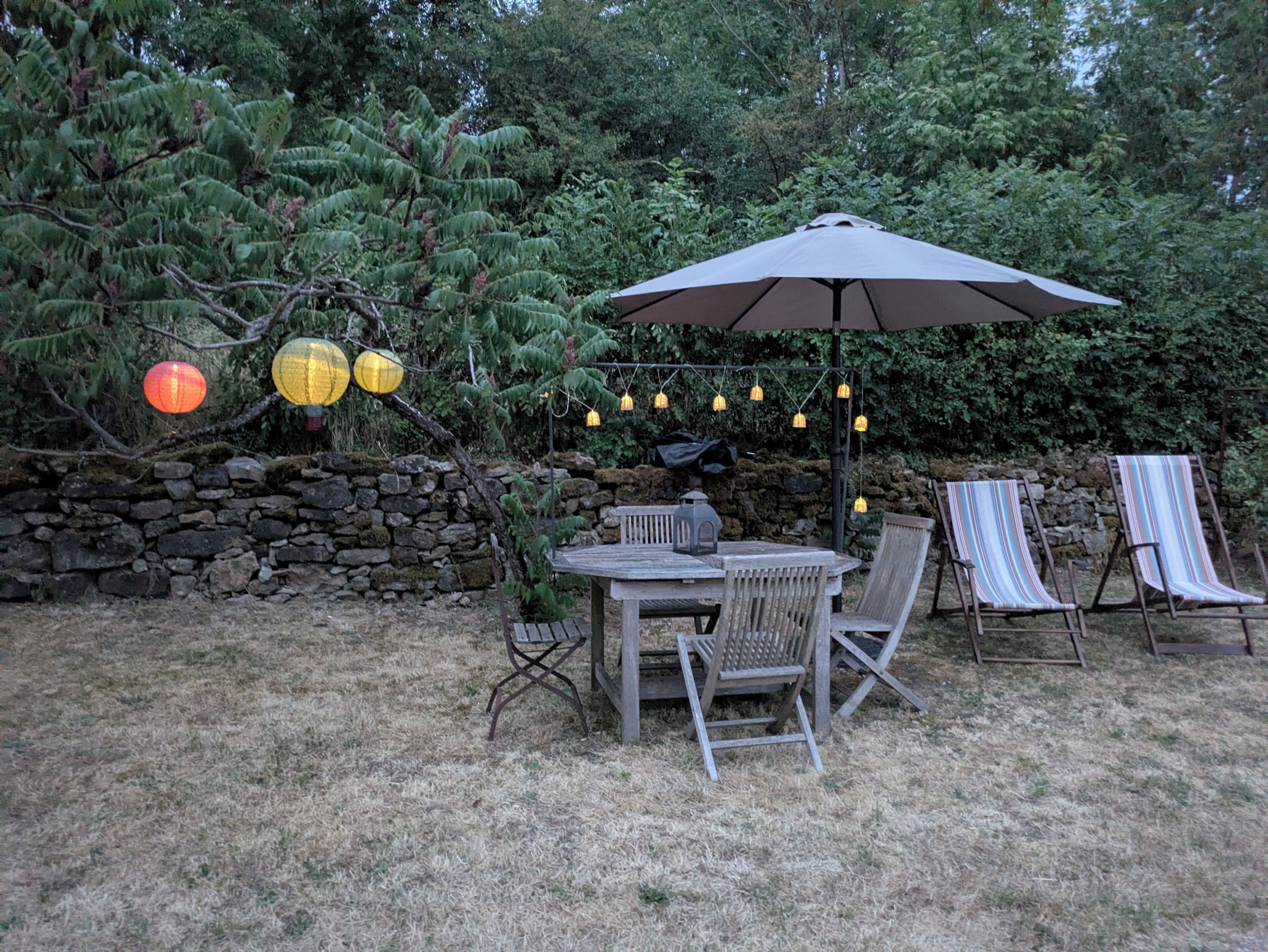 Une terrasse extérieure avec une table et des chaises, entourée d’un mur de pierre et de verdure.