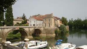 Un río con un puente de piedra, barcos amarrados en un muelle y edificios al fondo.