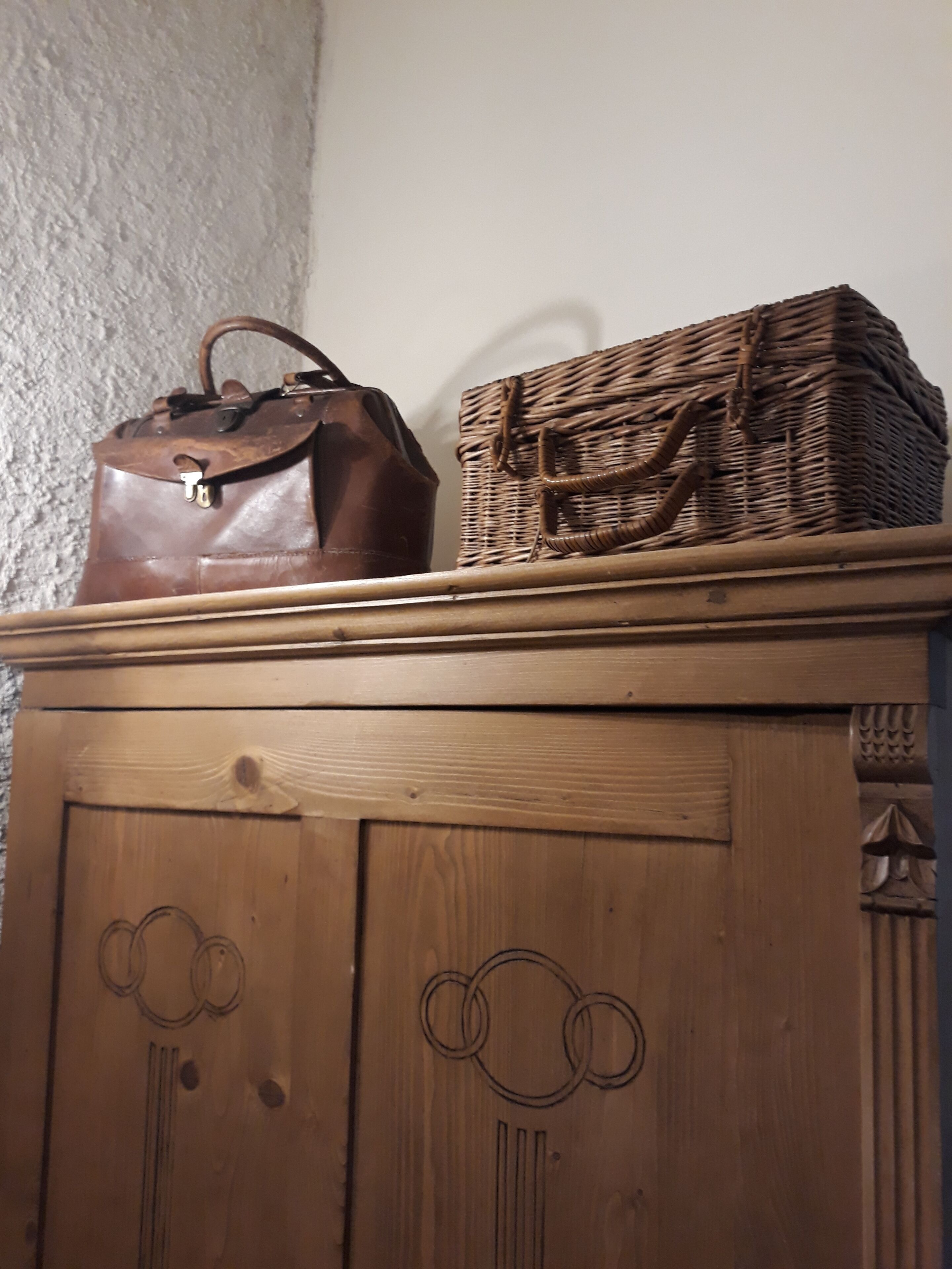 A wooden cabinet with a woven basket and a brown leather bag on top.