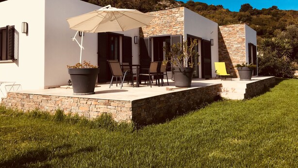 A modern outdoor patio with stone walls, a white building, and a large umbrella.