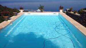 A rectangular swimming pool with clear blue water, surrounded by stone walls and potted plants.