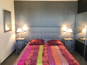 Une chambre à coucher avec un grand lit, deux tables de chevet avec des lampes, un miroir et une tête de lit.