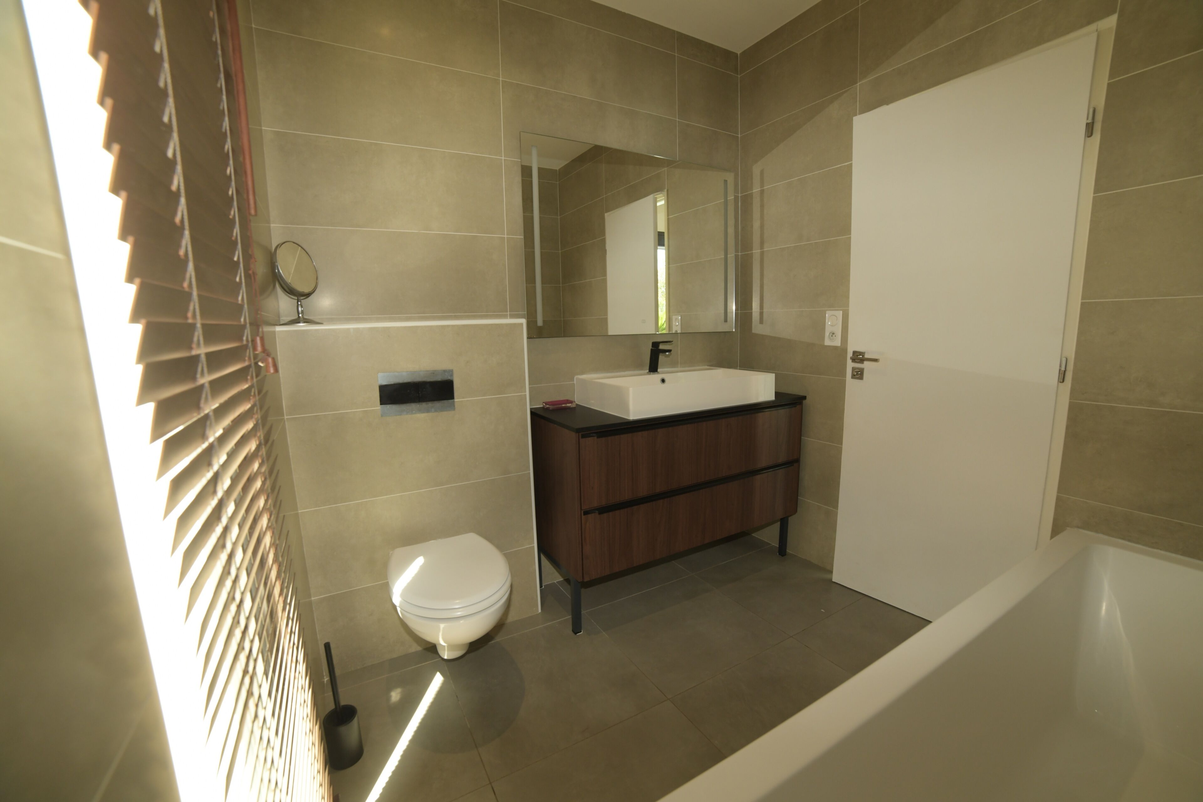 Een moderne badkamer met toilet, wastafel, spiegel en bad.