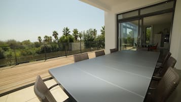 Een moderne eethoek buiten met een lange tafel en stoelen, met uitzicht op een tuin met palmbomen.