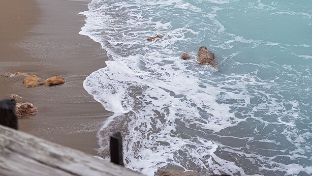 A coastal beach scene with waves crashing onto the shore, rocky outcrops, and a wooden fence. - SETE, listed villa 240 m2, 50 meters from the beach, 1st sea line, swimming pool (Sète)
