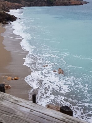 Una spiaggia costiera con onde che si infrangono sulla riva, affioramenti rocciosi e una recinzione in legno.