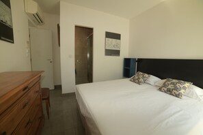 A bedroom with a bed, a wooden dresser, a shower, and a wall-mounted air conditioner.