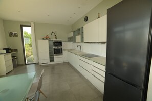 A modern kitchen with white cabinets, a black refrigerator, and a dining area with a glass table.