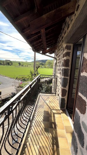 A balcony with a view of a green field and a stone wall.