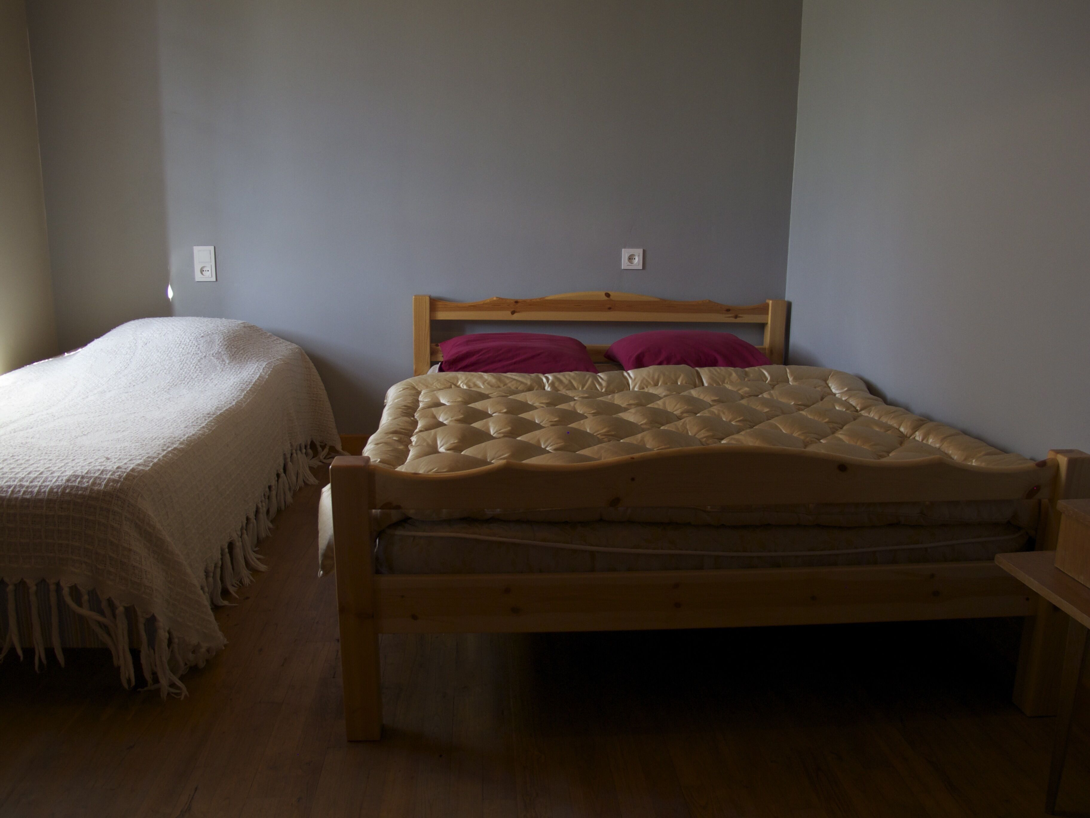 A single bed with a wooden frame and a quilted mattress. There is a wooden nightstand to the right of the bed.