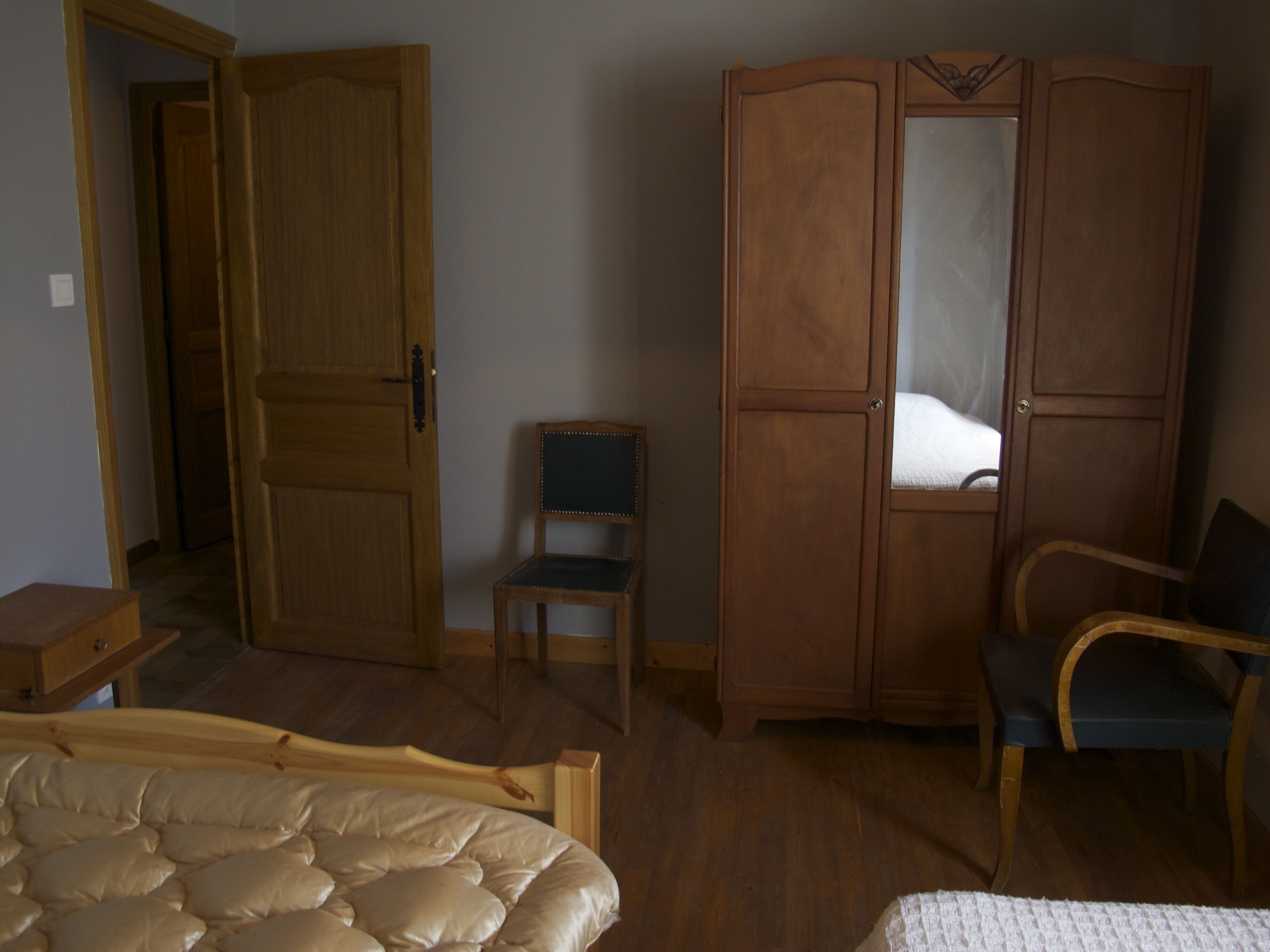 A room with a bed, a wooden wardrobe, a chair, and a small table.