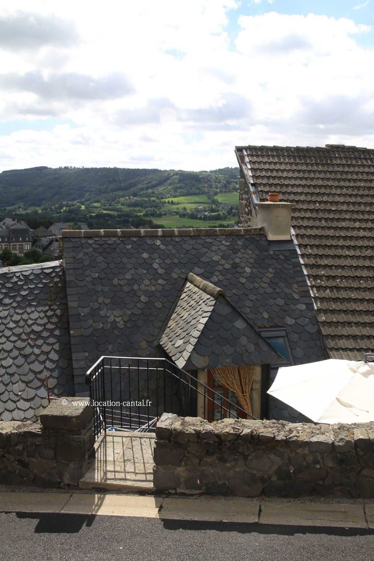 A stone staircase leading to a rooftop with a view of a green valley and hills.