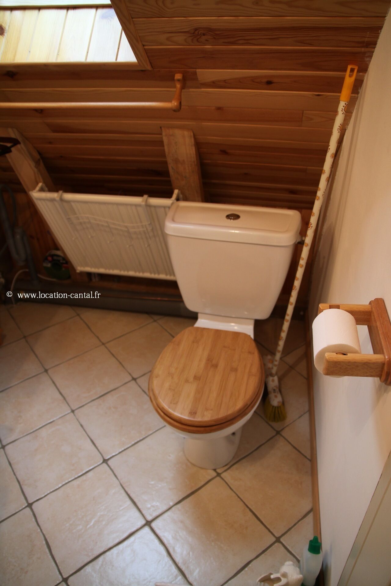 Des toilettes en bois, avec un abattant et un couvercle en bois, une cuvette blanche et un porte-rouleau de papier toilette fixé au mur.