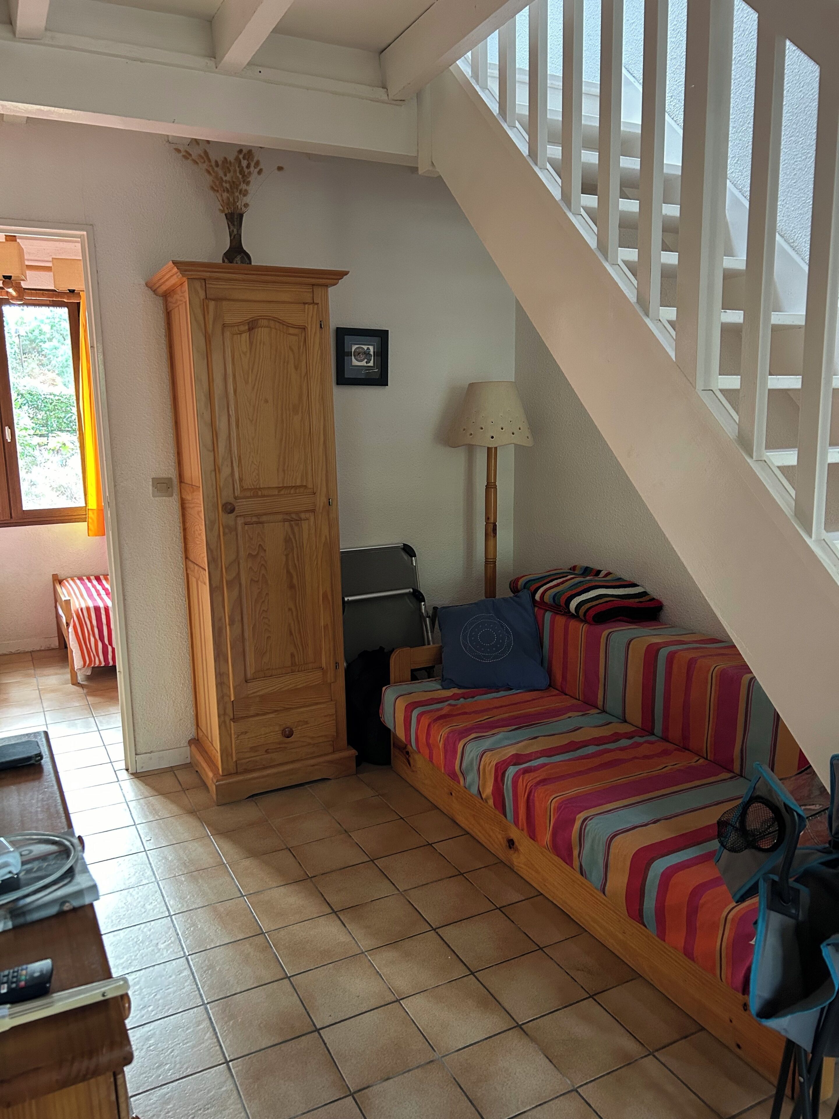 Une pièce chaleureuse avec une armoire en bois, un canapé rayé aux couleurs vives, une lampe et un escalier offrant une vue agréable.