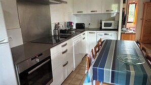 A compact kitchen with white cabinets, a stainless steel range, and a dining table with a striped tablecloth.