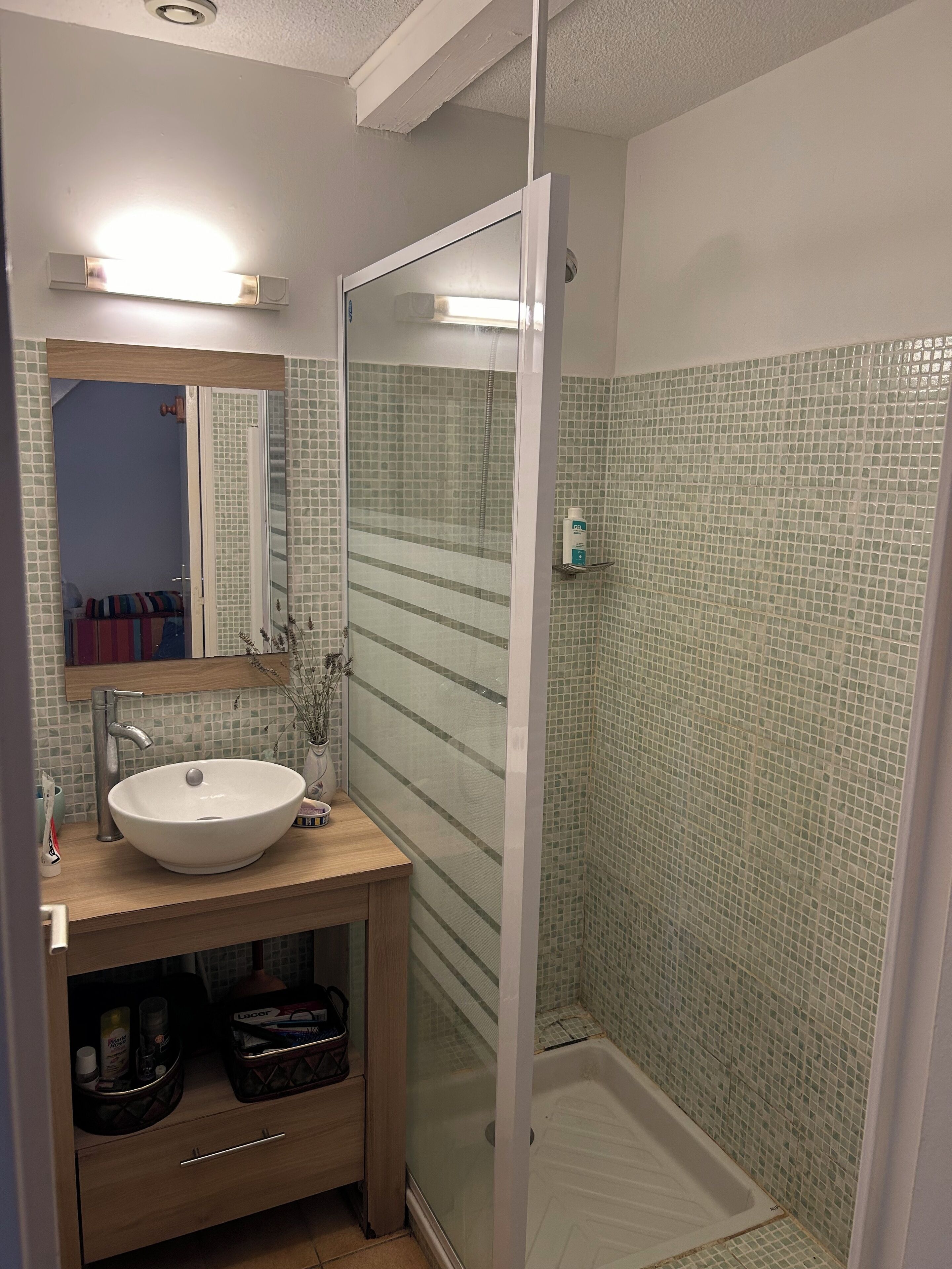 Une salle de bain avec une douche à parois de verre, un lavabo avec un miroir au-dessus et un mur recouvert de carreaux.