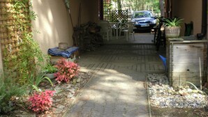 A covered outdoor area with a car parked in the background, a wooden bench, and a potted plant.