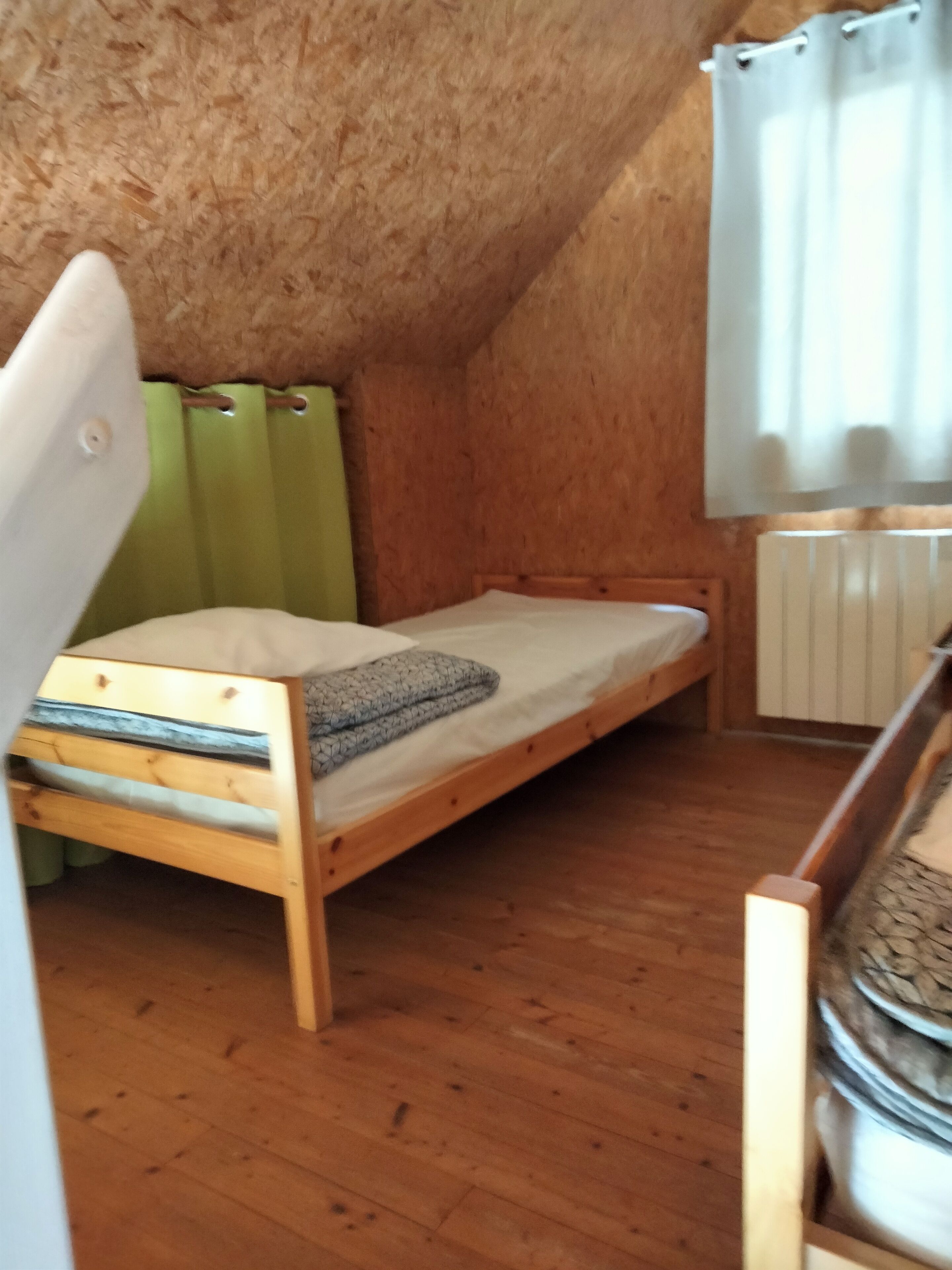 Une petite chambre avec un lit simple, des murs en bois et un plafond en pente.