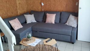 Un salon moderne avec un canapé d’angle gris, une table basse en bois et un luminaire blanc au plafond.
