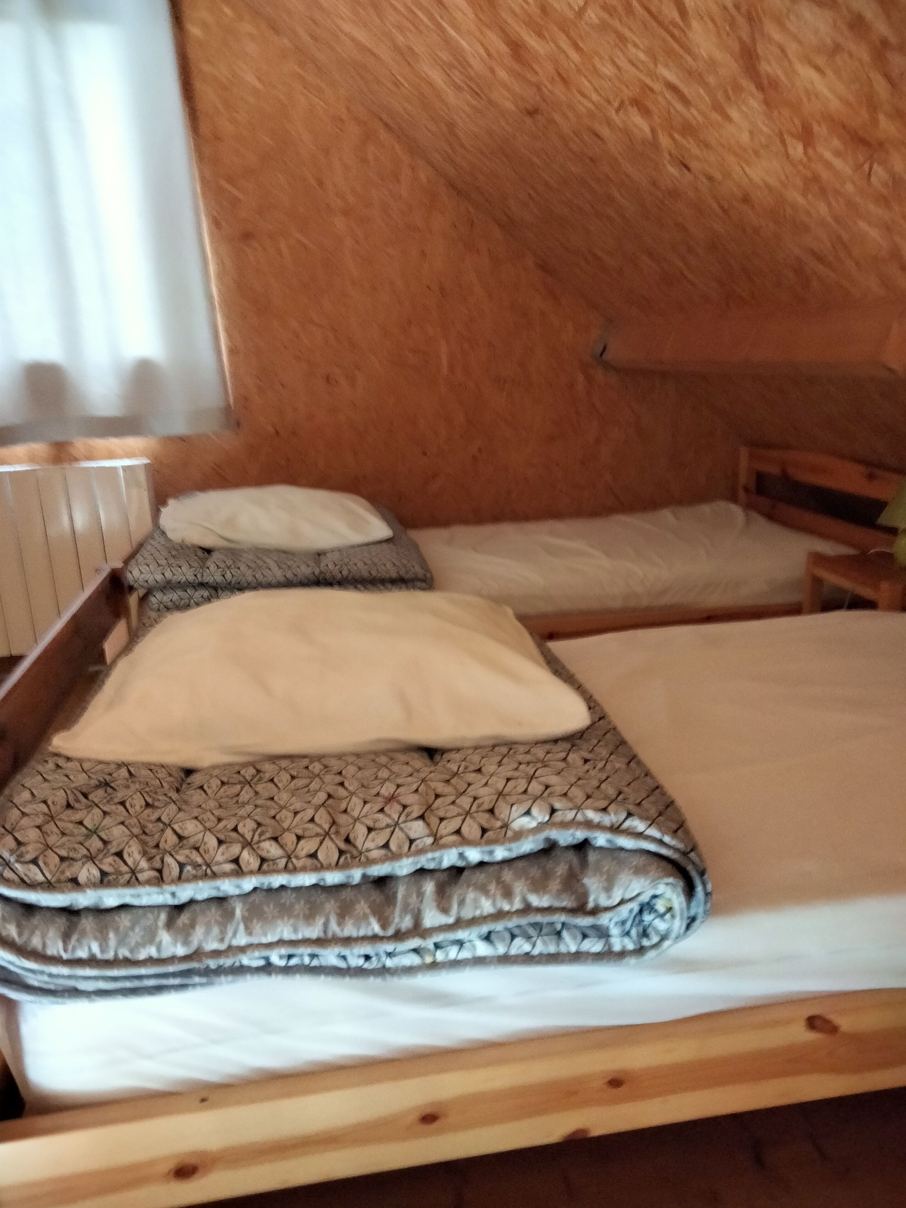 Un pequeño y acogedor dormitorio en ático con techo inclinado de madera, dos camas individuales con ropa de cama estampada y un radiador a la izquierda.