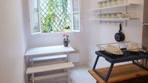 Une cuisine avec une fenêtre, des étagères blanches ornées de bocaux, une cuisinière et un banc.