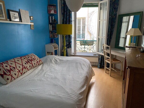 Een slaapkamer met een bed, een bureau en een stoel. Er is een raam met uitzicht op het buiten.