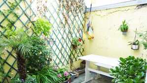 Un petit espace extérieur avec un banc blanc, diverses plantes en pot et une clôture en treillis bleue.