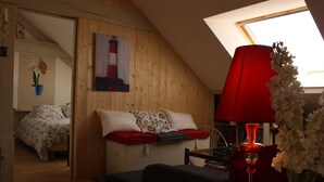 Um quarto aconchegante com teto inclinado, uma cama com roupa de cama florida, um abajur vermelho e um quadro de um farol.