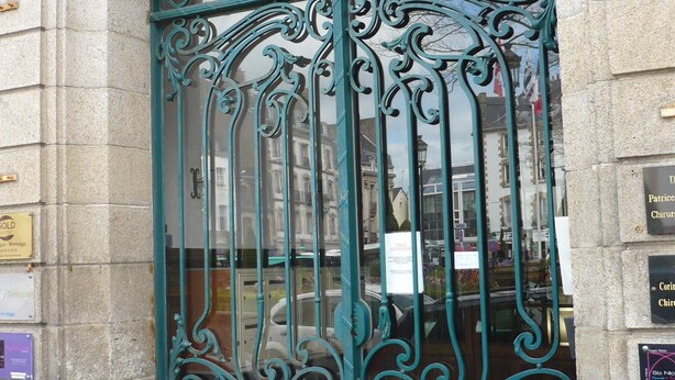 Entrada de um edifício histórico com portões de ferro ornamentados e um arco de pedra.