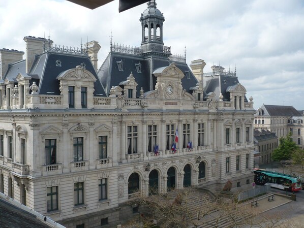 A historic building with classical architecture, featuring multiple windows, a prominent clock tower, and flags.