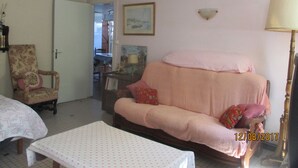 Un salon confortable avec un canapé, un fauteuil et une table. Une porte donne accès à une autre pièce, et une lampe est posée sur une table d’appoint.