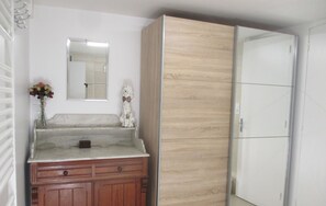 A room with a wooden cabinet, a mirror, a small statue, and a white wardrobe. - Bright, comfortable 2/5-person apartment, private garden, barbecue, garden furniture. (Mimizan)