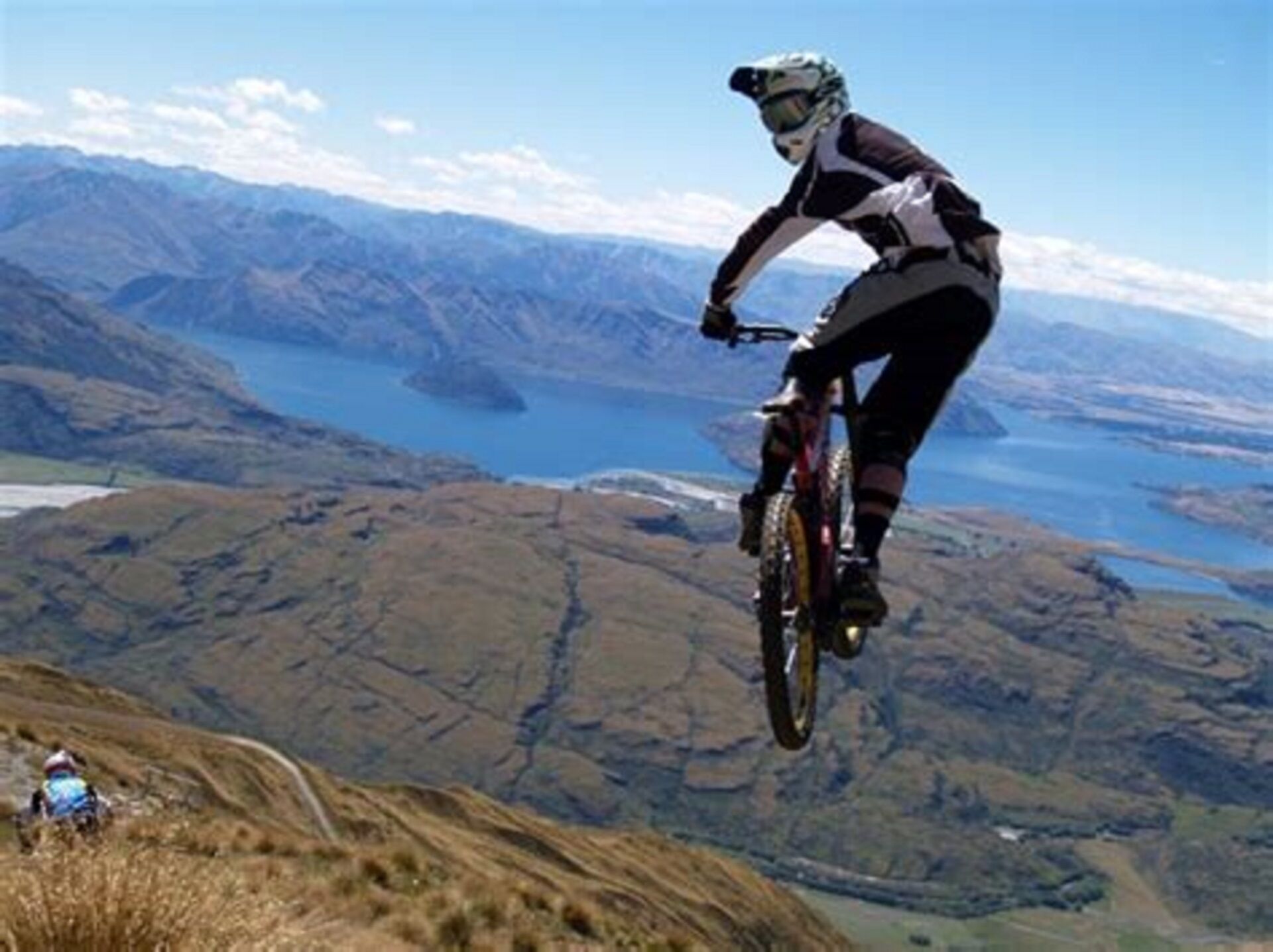 Een mountainbiker in de lucht boven een pittoresk landschap met bergen en een meer.