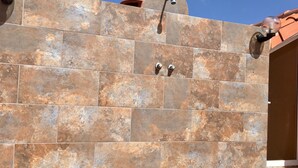Un mur recouvert de carreaux, avec une pomme de douche et deux robinets.
