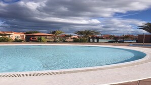 Une grande piscine aux eaux claires, à bords incurvés, entourée d’une terrasse dallée.