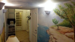 A hallway with a door leading to a room, a small shelf with items, and a mural of a landscape. - Large house in Sernhac (Sernhac)