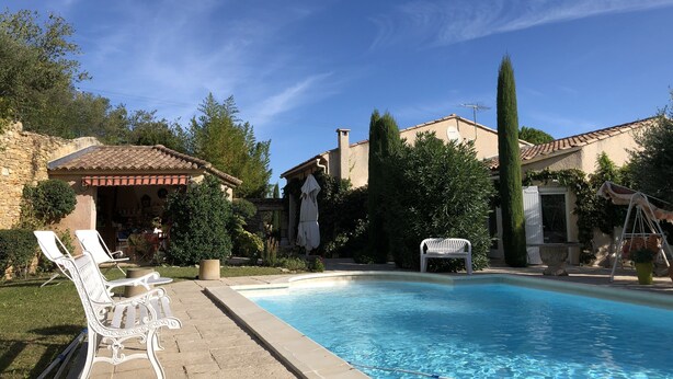 A swimming pool with lounge chairs, a stone wall, and a building with a tiled roof. - Large house in Sernhac (Sernhac)