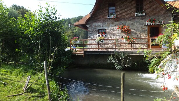 A stone building with a wooden balcony, a river in front, and a bridge.