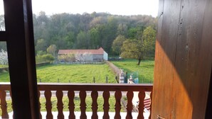 A balcony with a view of a green field, a building with a red roof, and a statue.