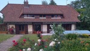 A two-story house with a tiled roof, a front porch, and a garden with various flowers.