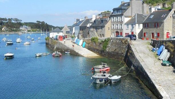 Un pueblo costero con edificios de piedra, un puerto con barcos y un muro de piedra a lo largo de la costa.